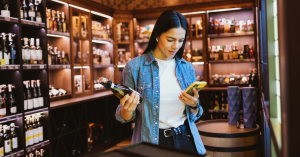 Woman browsing phone while holding wine bottle.